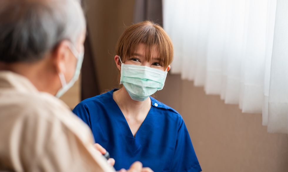 Image: Nurse with smiling eyes wearing a surgical mask and speaking to a man