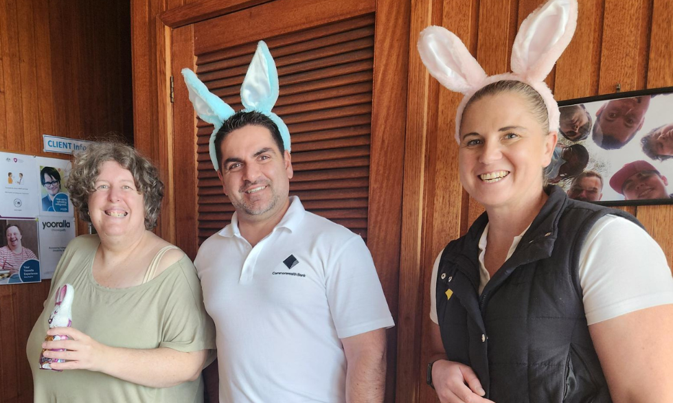 Image description: Yooralla client holding an Easter chocolate egg. Two bank staff members wearing bunny ears and holding a basket of chocolate eggs.