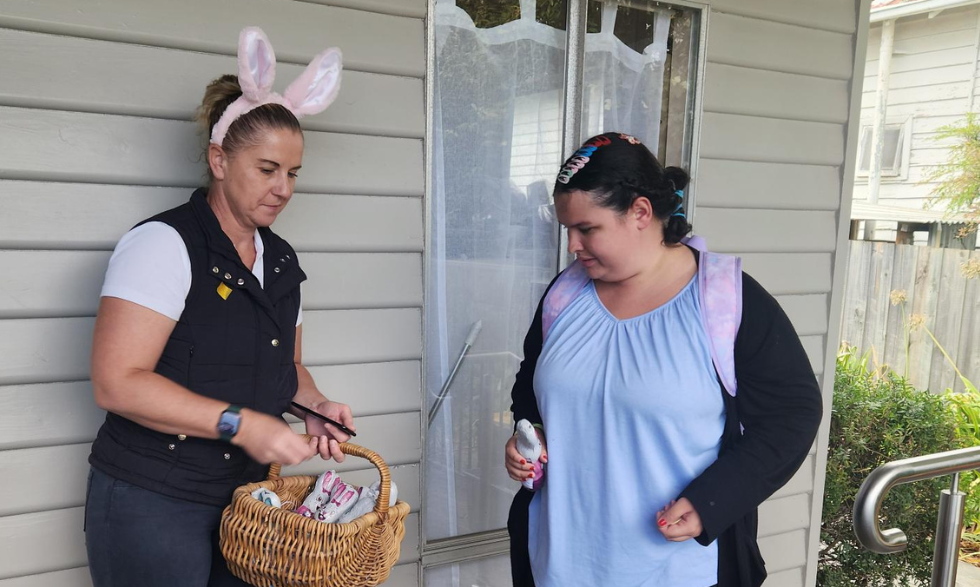 Image description: Bank staff member passing a chocolate to a Yooralla client. The staff member is wearing bunny ears and holding a basket of chocolate eggs.
