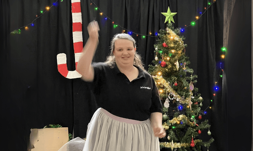 A Yooralla client performing a dance routine for a group - They are dancing infront of a candy cane decoration and christmas tree