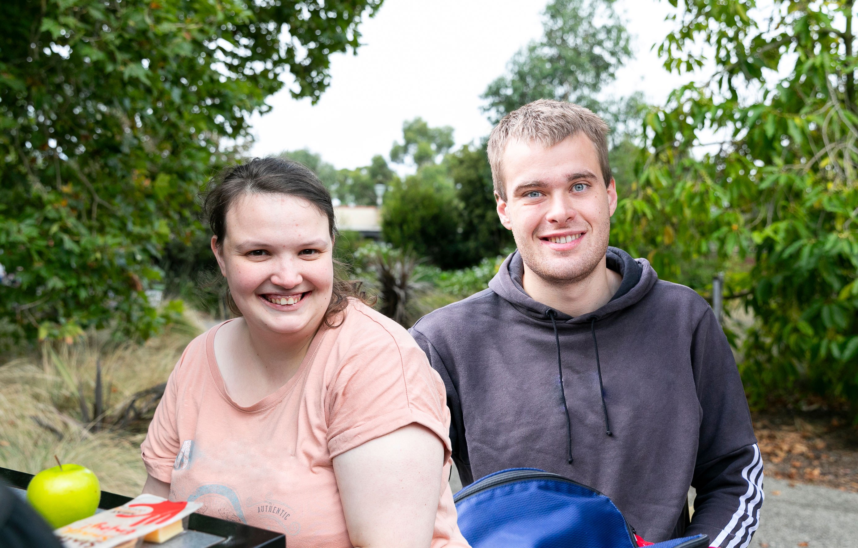 IMAGE: two clients with disability are in a park smiling to the camera