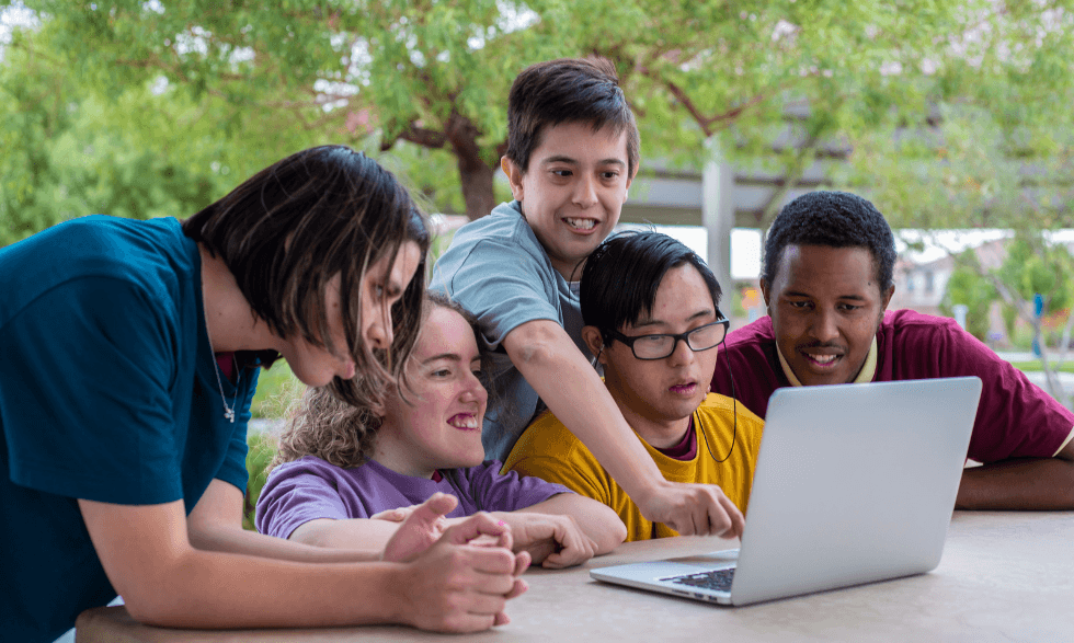 A group of people are huddled around a lap top sharing the Yooralla enews together