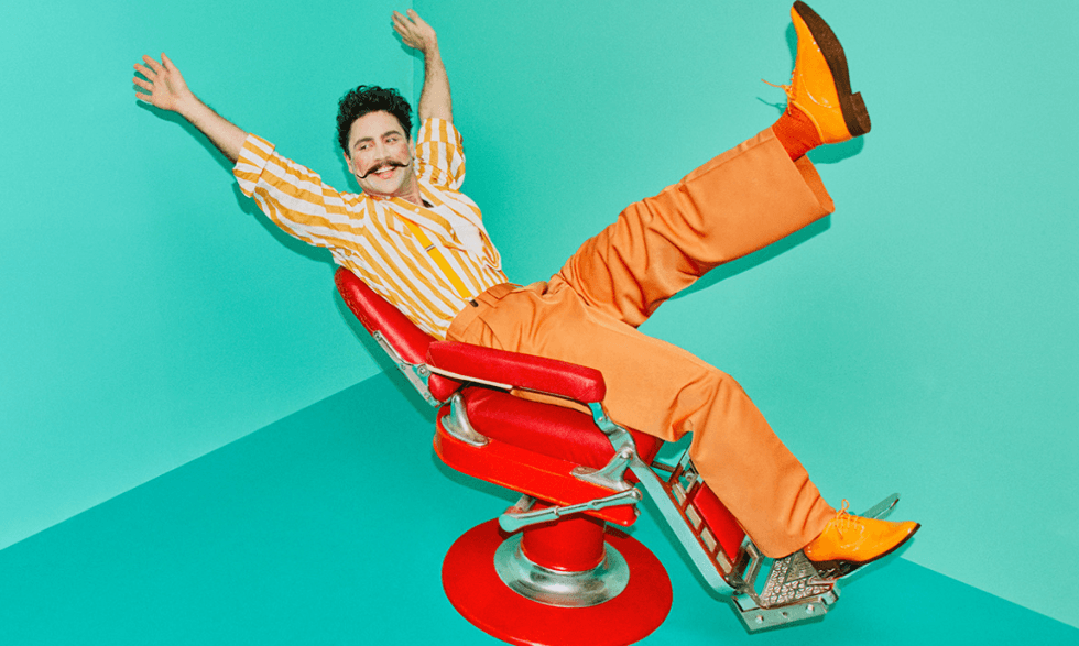 Official Image of Opera Australia's Barber of Saville - the barber is clothed in orange leaning back on a red barbers' chair