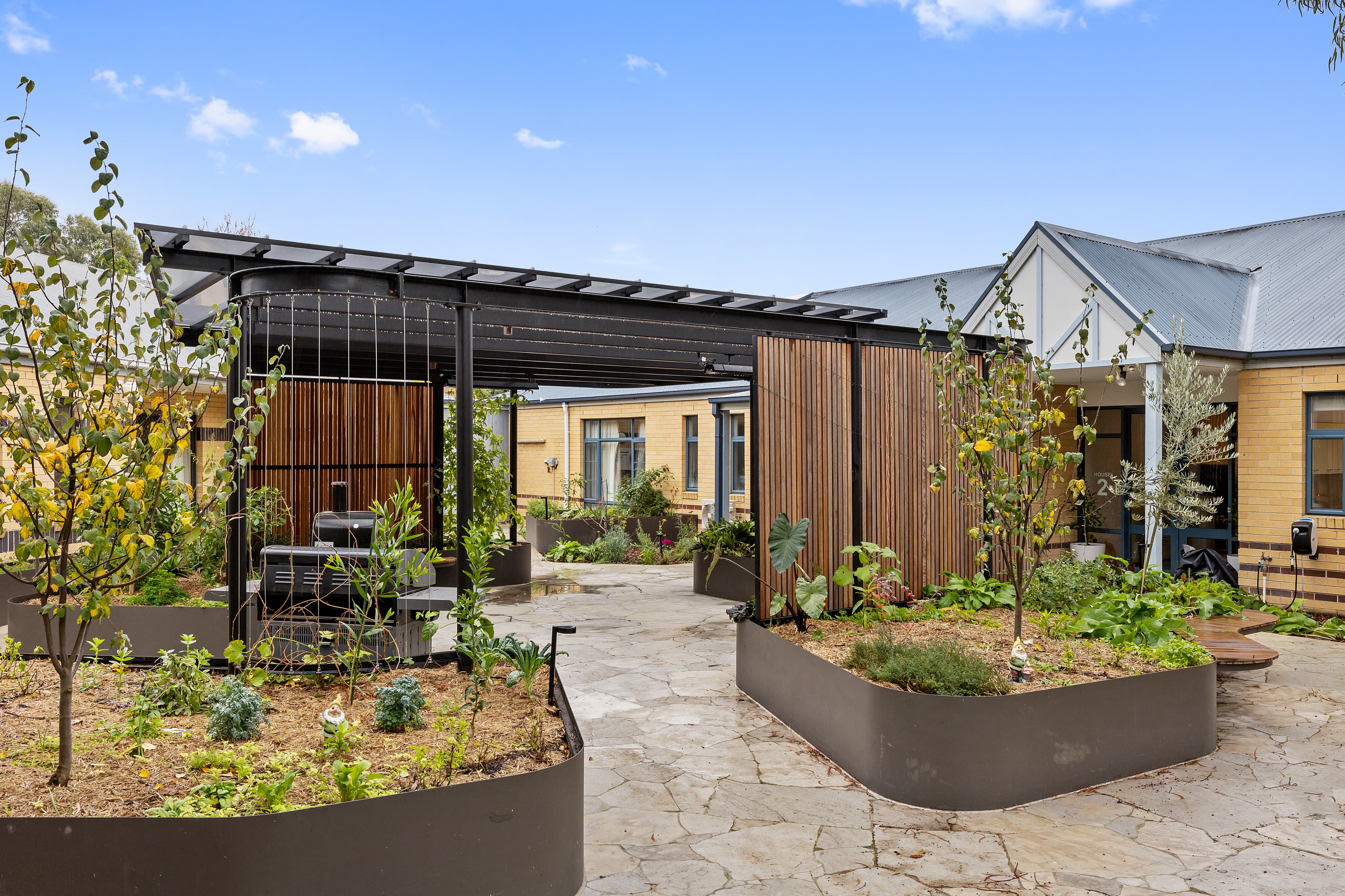 Image: Blue skies over Thornbury sensory garden. Raised beds with trees and shrubbery.