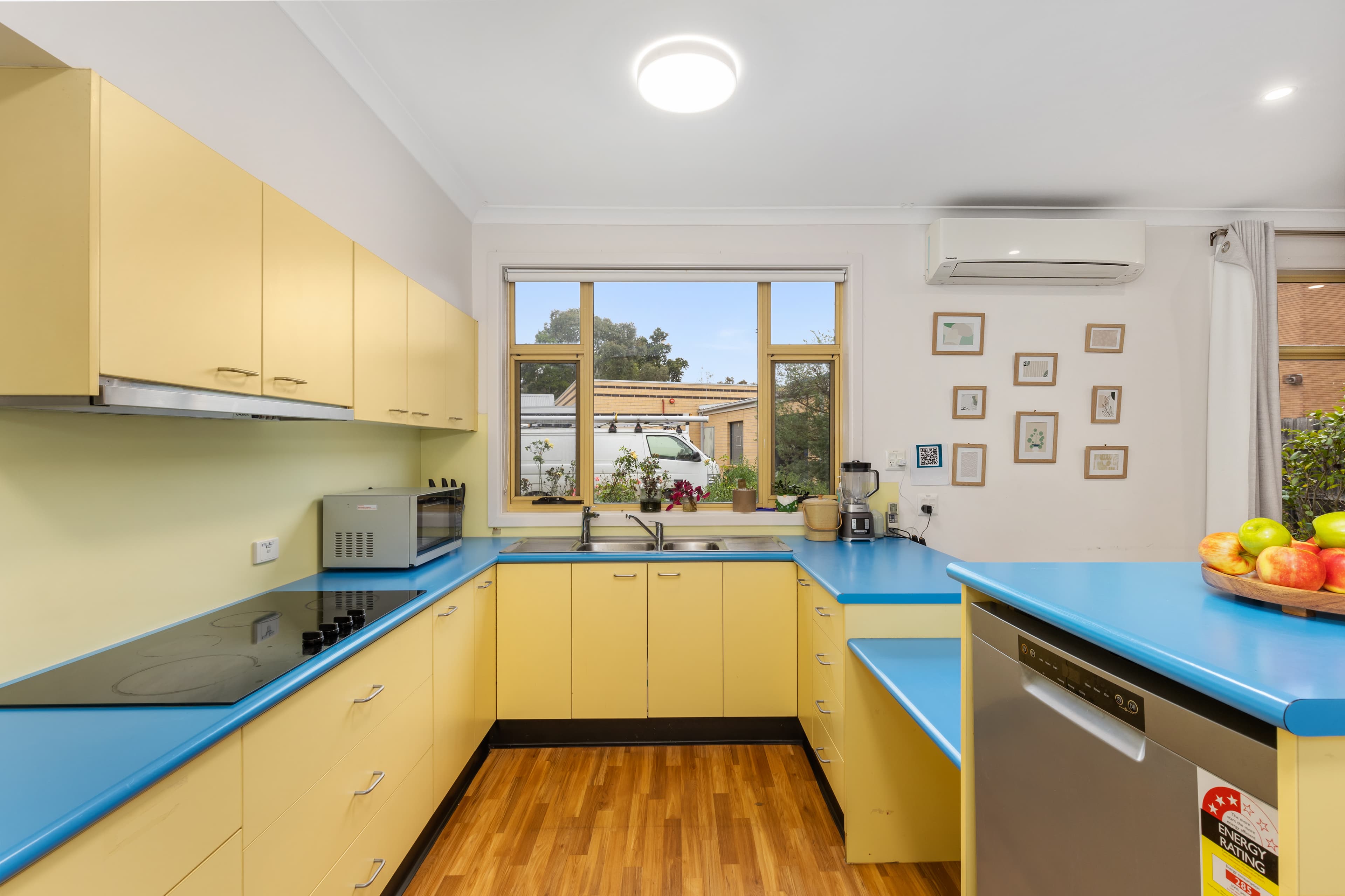 Image: Kitchen with wooden floors, yellow cabinetry and sky blue benchtops