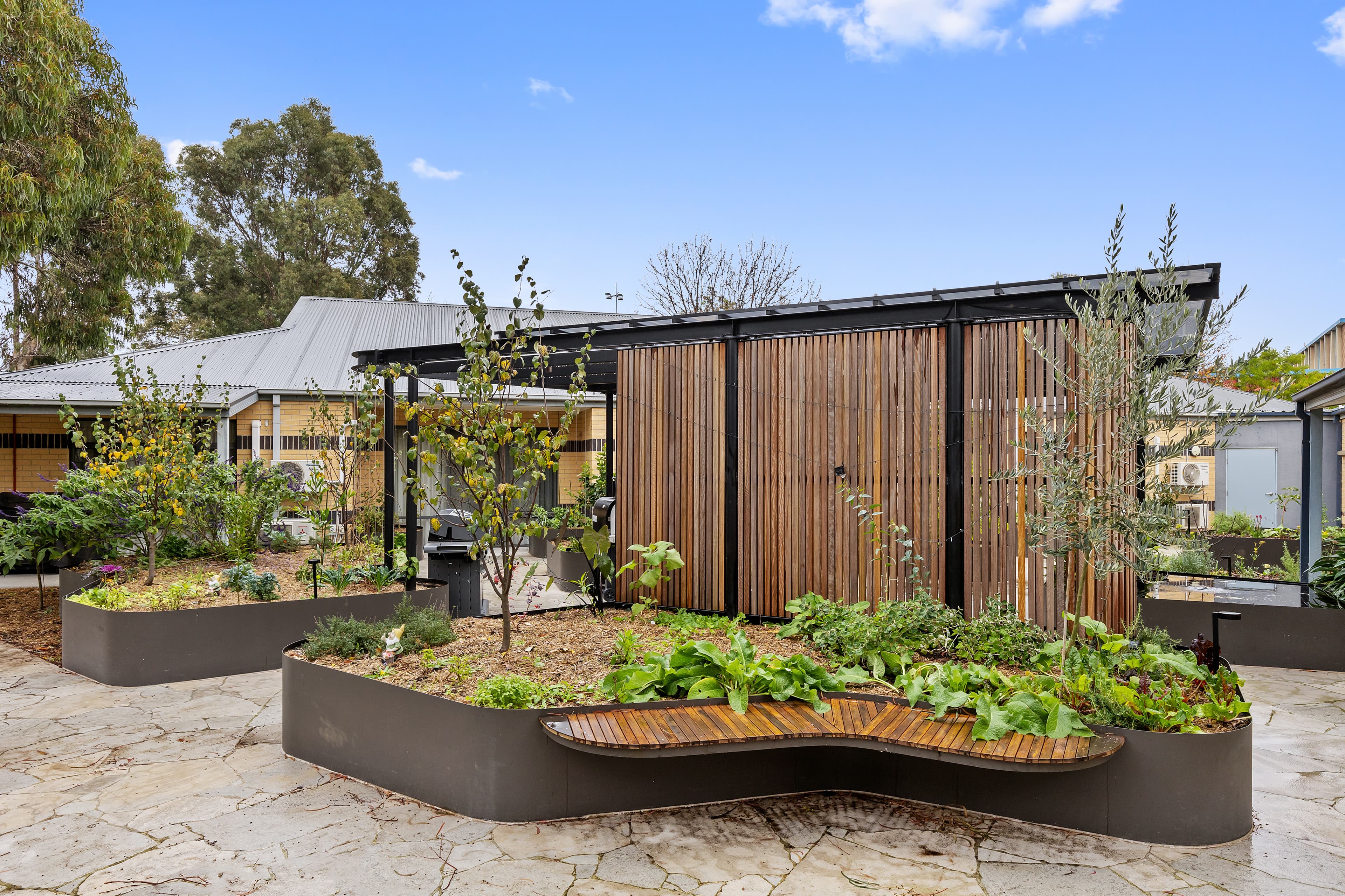 IMAGE: The outside of the Sensory Garden at Thornbury. Pictured are blue skies and a raised bed filled with mulch, plants and herbs.