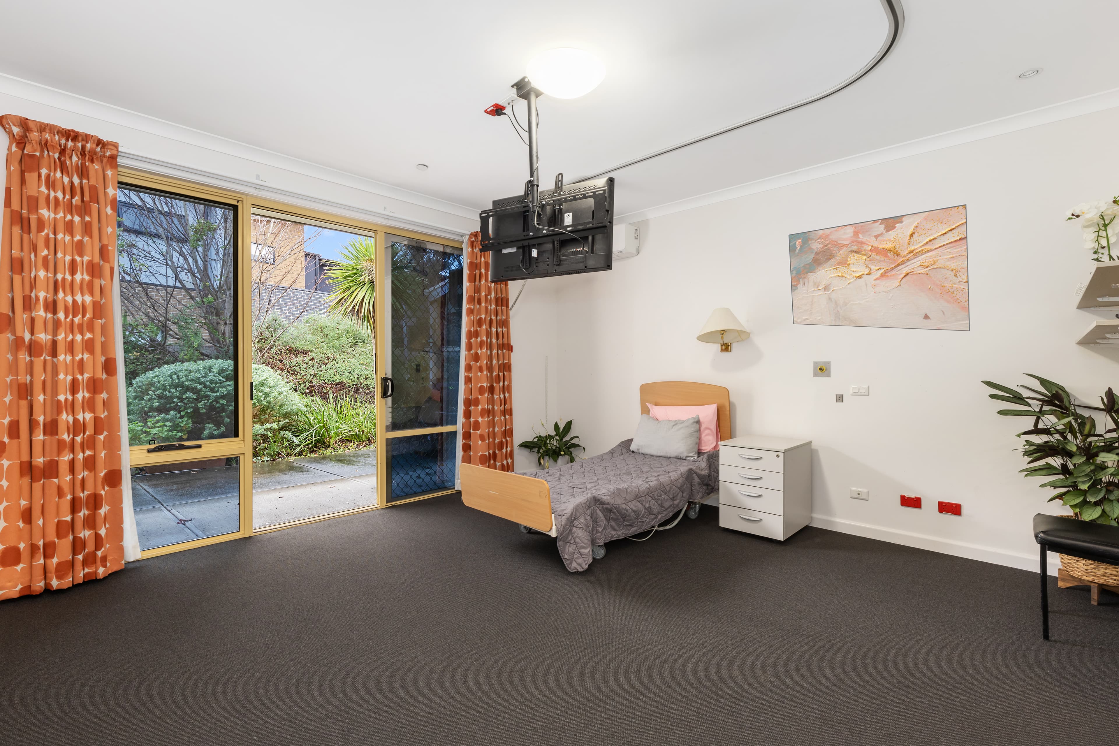 Image: A bedroom with grey carpet, orange curtains opening out onto the garden, and a bed.