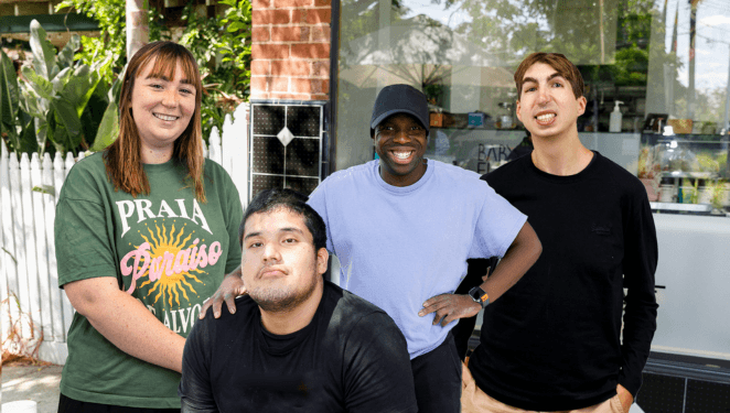 IMAGE: 4 clients from the Yooralla community hub are sitting together outdoors at a cafe and smiling to camera